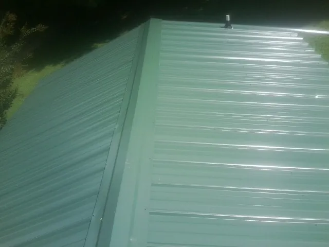 New green metal panels meeting at the ridge of a roof — Flat Roof Repair work by our crew in Hebron